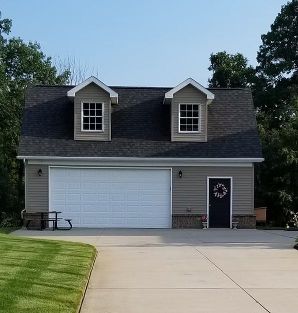Two-story gray garage with white garage door, two dormers, and a black door with a wreath.