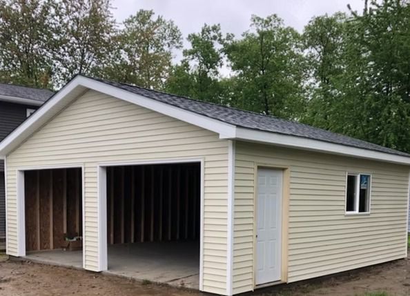 Two-car garage with tan siding, gray roof, and a white door and window.