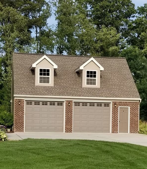 Two-car garage with brown doors and roof, brick accents, and two dormers. Set on a green lawn.