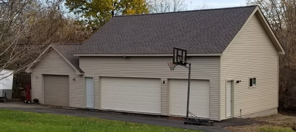 A tan house with a dark roof, three garage doors, and a basketball hoop on a concrete pad.