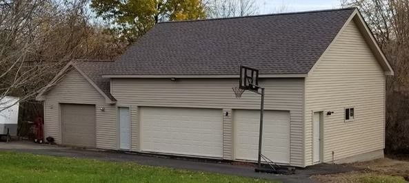 Tan building with garage doors, a basketball hoop, and a dark roof. Set in a grassy area.