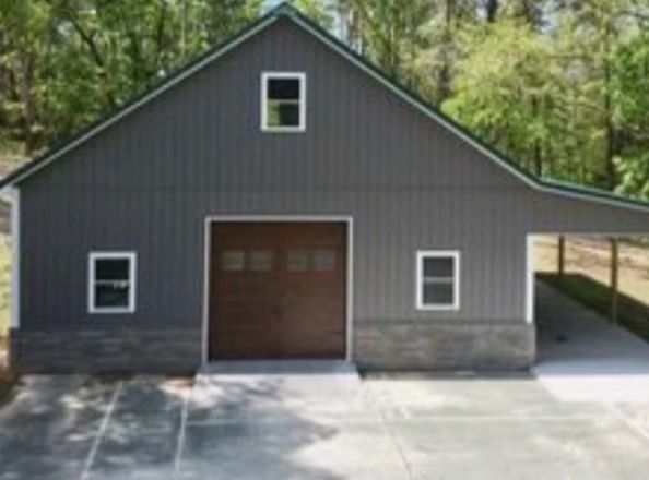 Gray barn-style building with brown garage door, stone base, and carport.