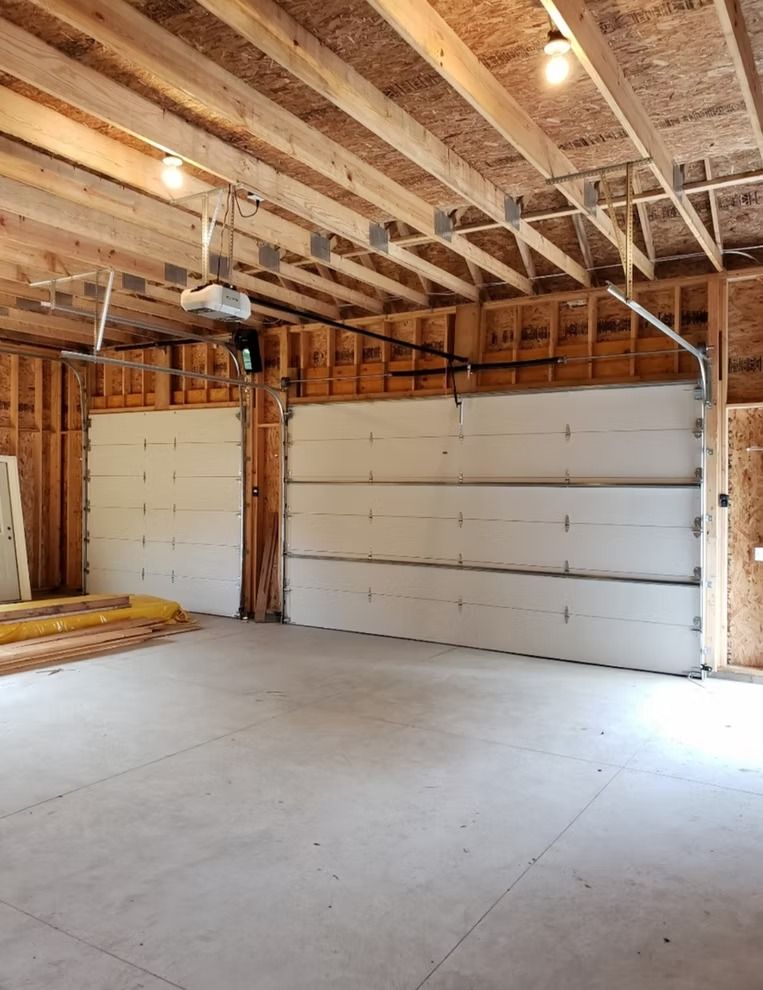 Framed garage interior with two white garage doors; concrete floor and exposed wooden beams.