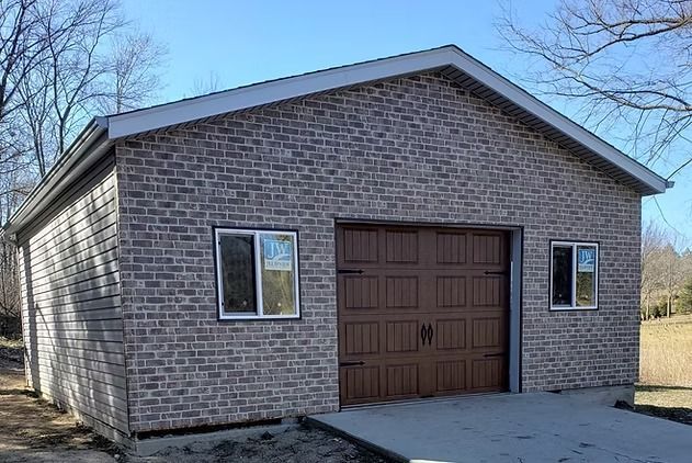 Brick-faced garage with brown door and windows; blue sky, trees in the background.