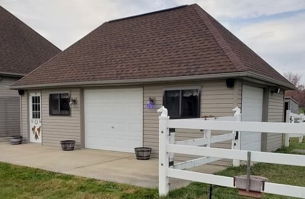 Tan building with brown roof, white garage doors and fence, two windows, and a white door.
