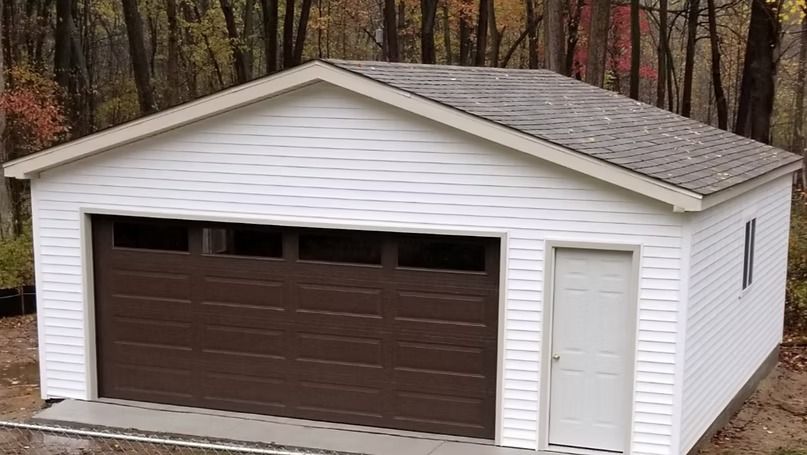 White garage with brown door, roof, and trim; small white door on side.