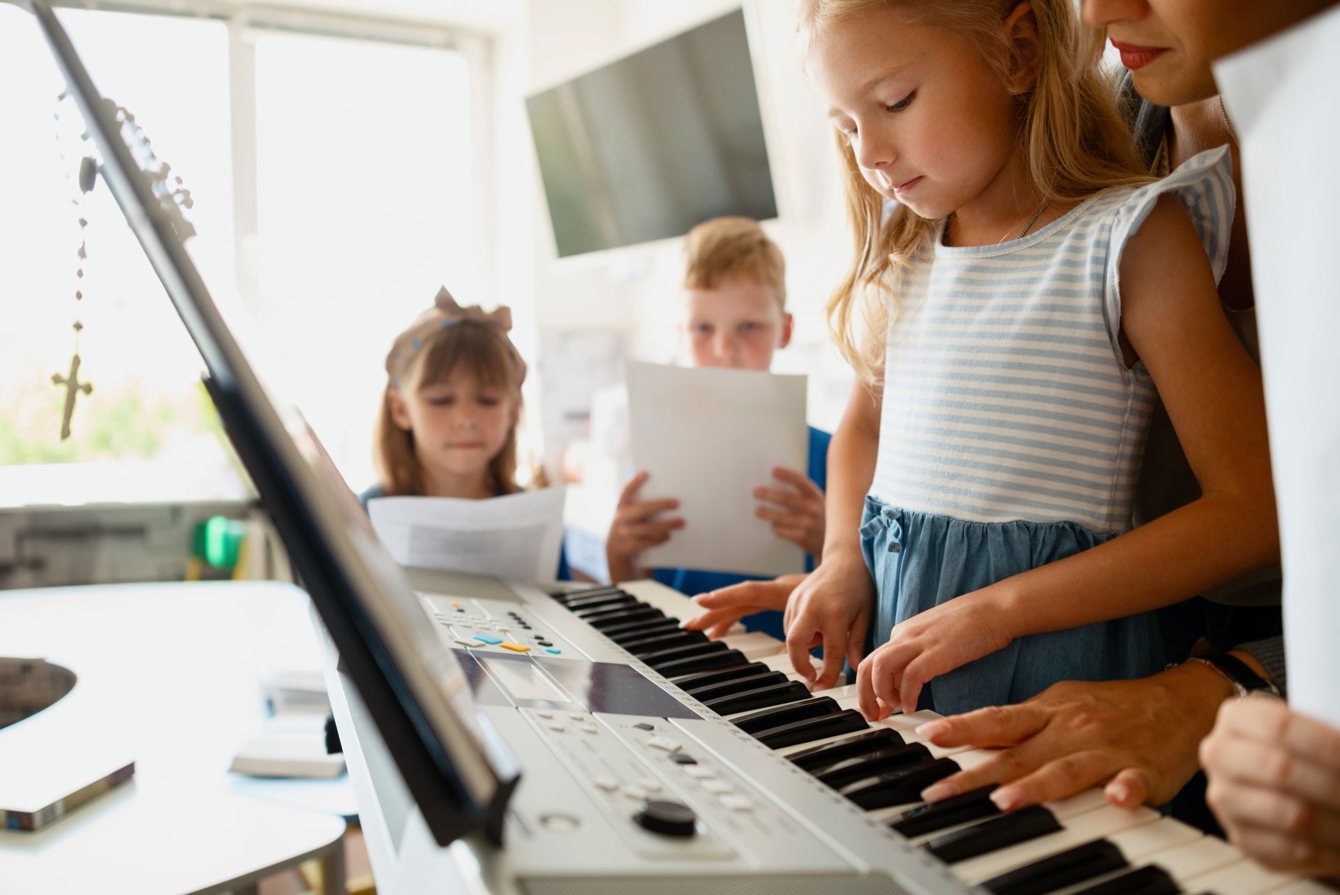 Girl playing keyboard with teacher and other children singing.