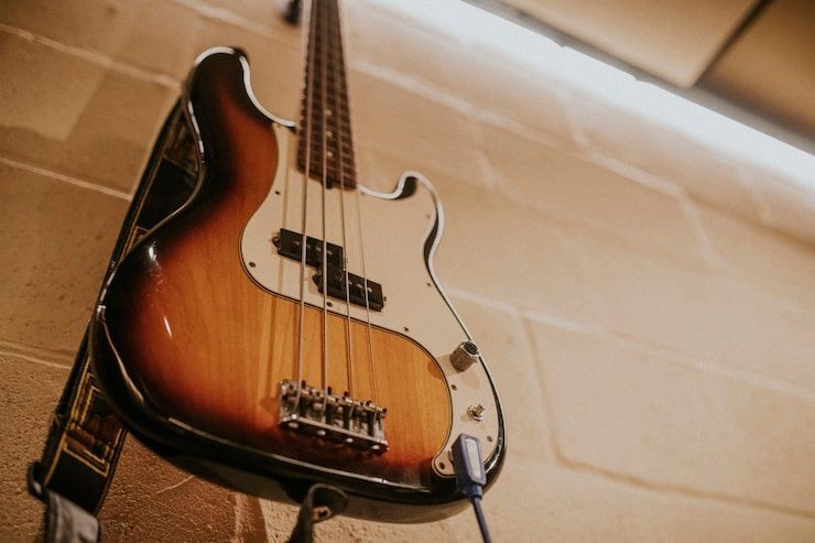 Sunburst bass guitar hanging on a brick wall with black strap and cable.