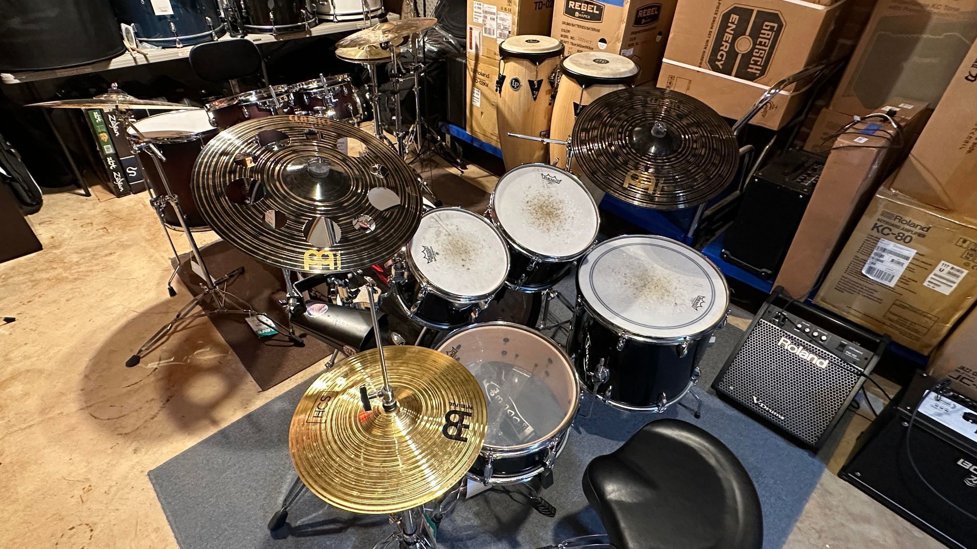Drum set with cymbals and hardware in a room; a stool is in front.