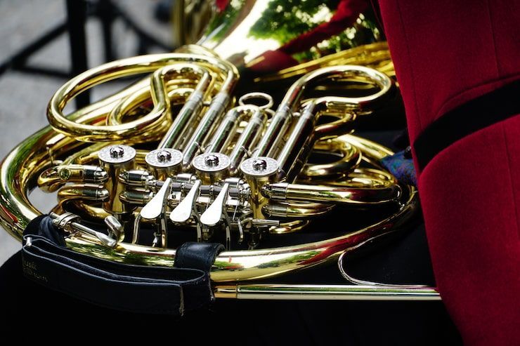 Close-up of a shiny, golden French horn with silver valves. Red uniform sleeve is visible.