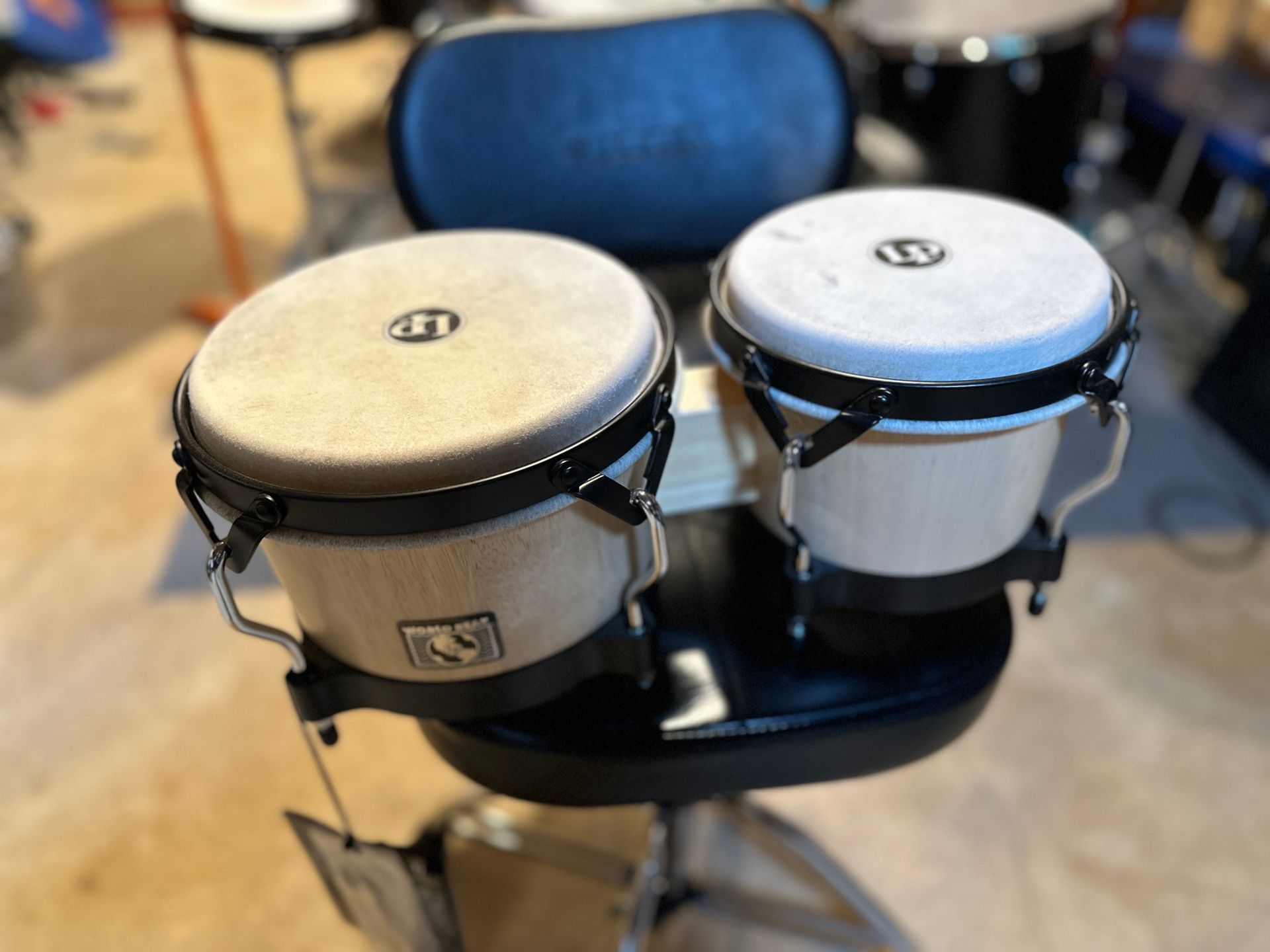 Bongo drums with light-colored heads, mounted on a black stool.