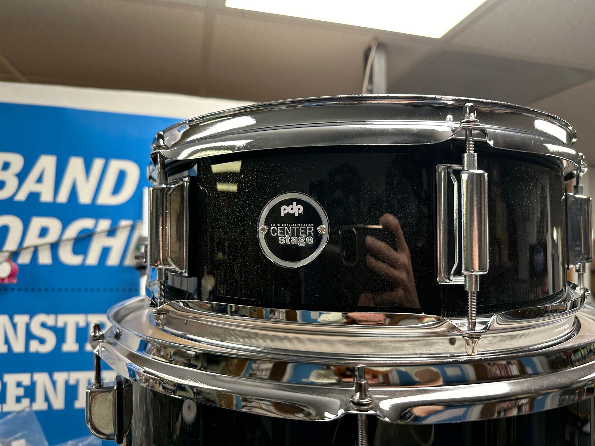 Black drum with silver hardware, PDP brand, in a music store.