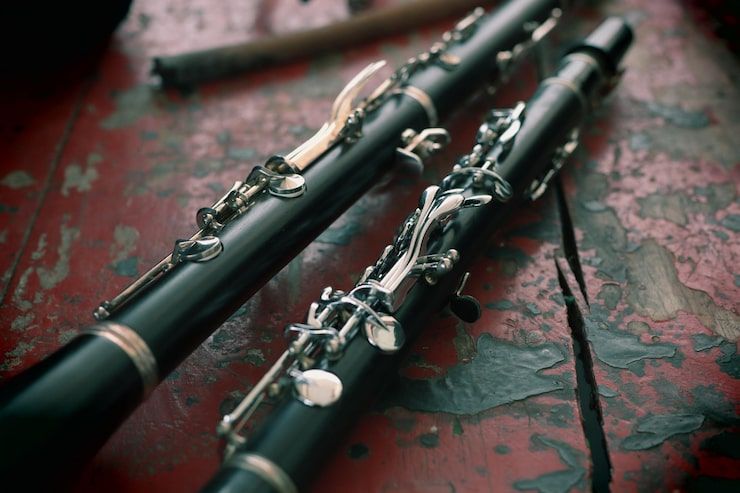 Two black clarinets with silver keys on a red, weathered surface.