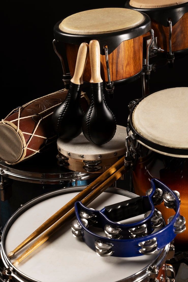 Assorted percussion instruments: drums, tambourines, maracas, and drumsticks on a dark surface.