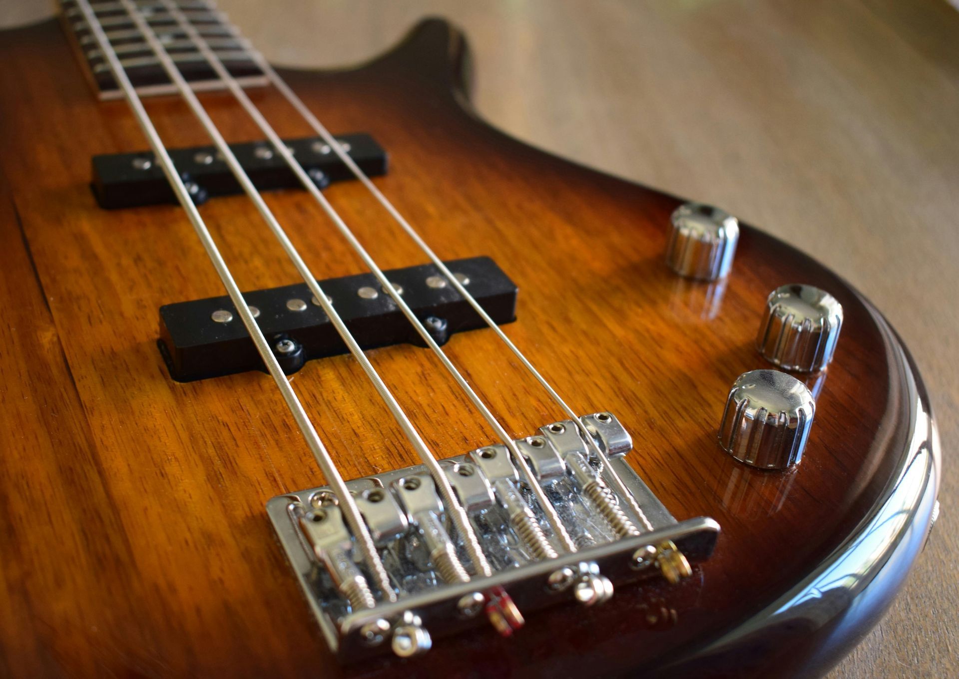 Close-up of a brown and tan bass guitar, with strings and chrome hardware, on a wood surface.