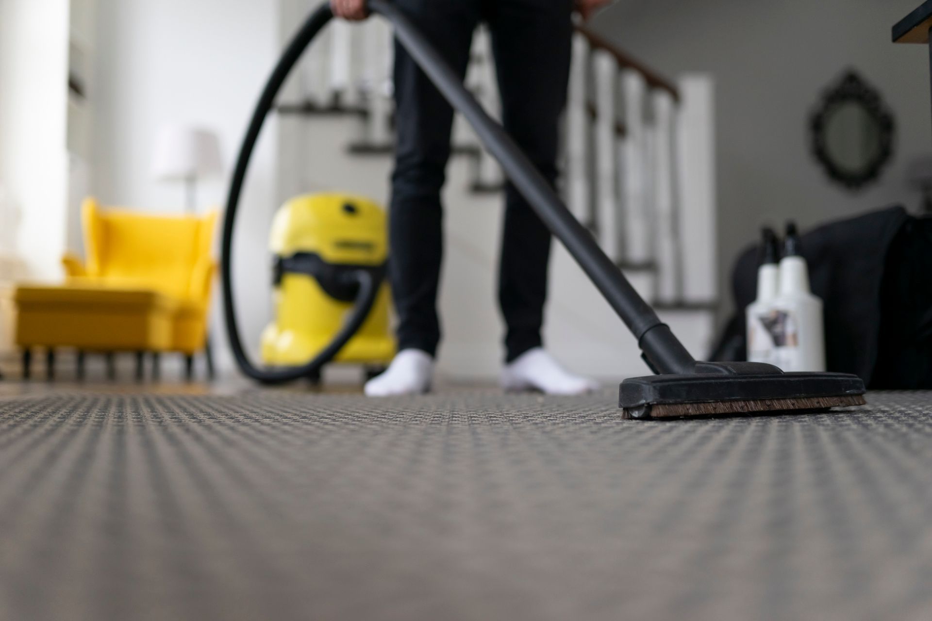 A man uses a vacuum cleaner on a carpet, highlighting the need to find carpet cleaning company.