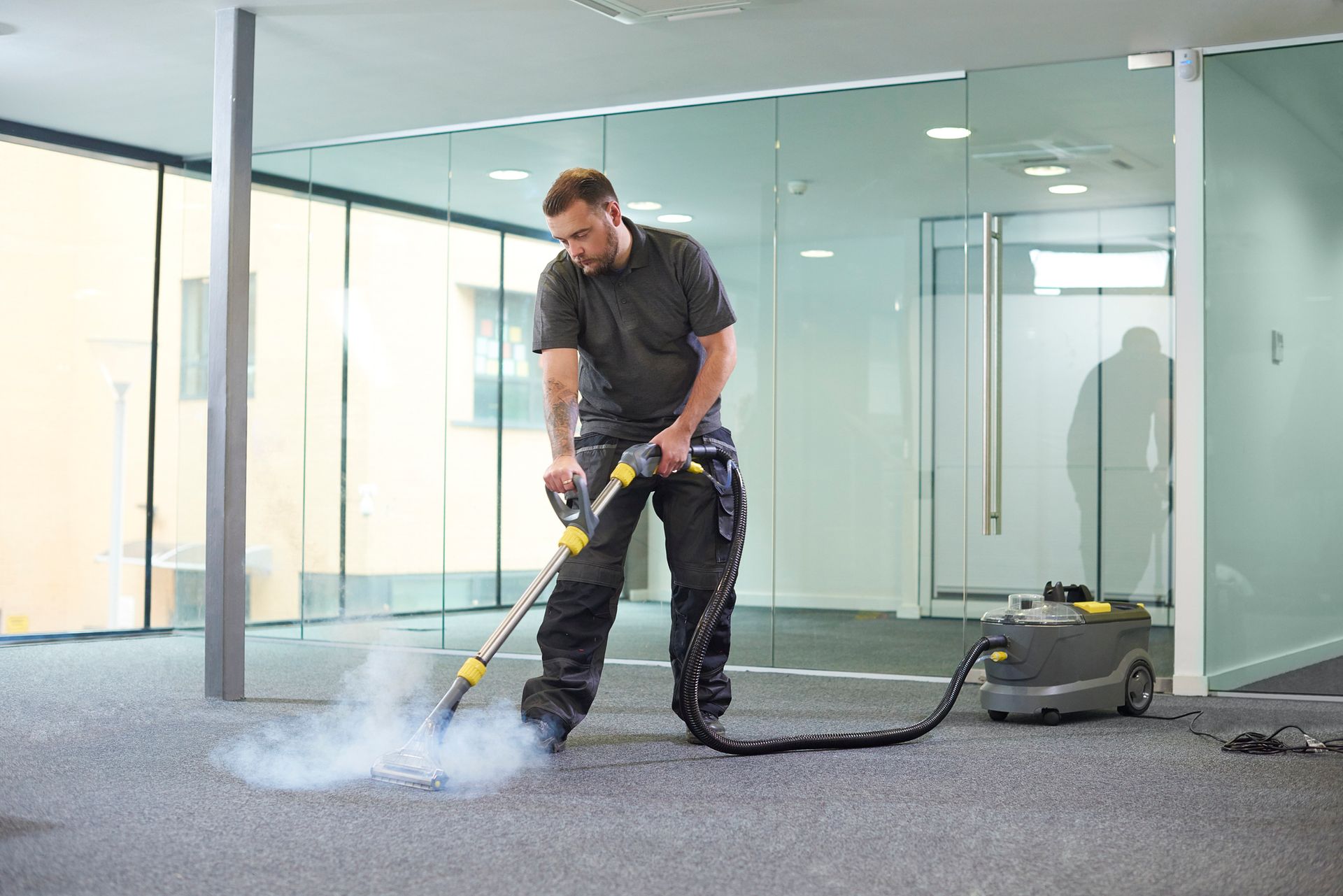 A male worker providing carpet cleaning service with a steam extractor in modern office space.
