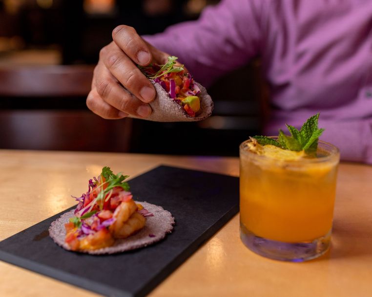 A person is eating a taco next to a drink on a table.