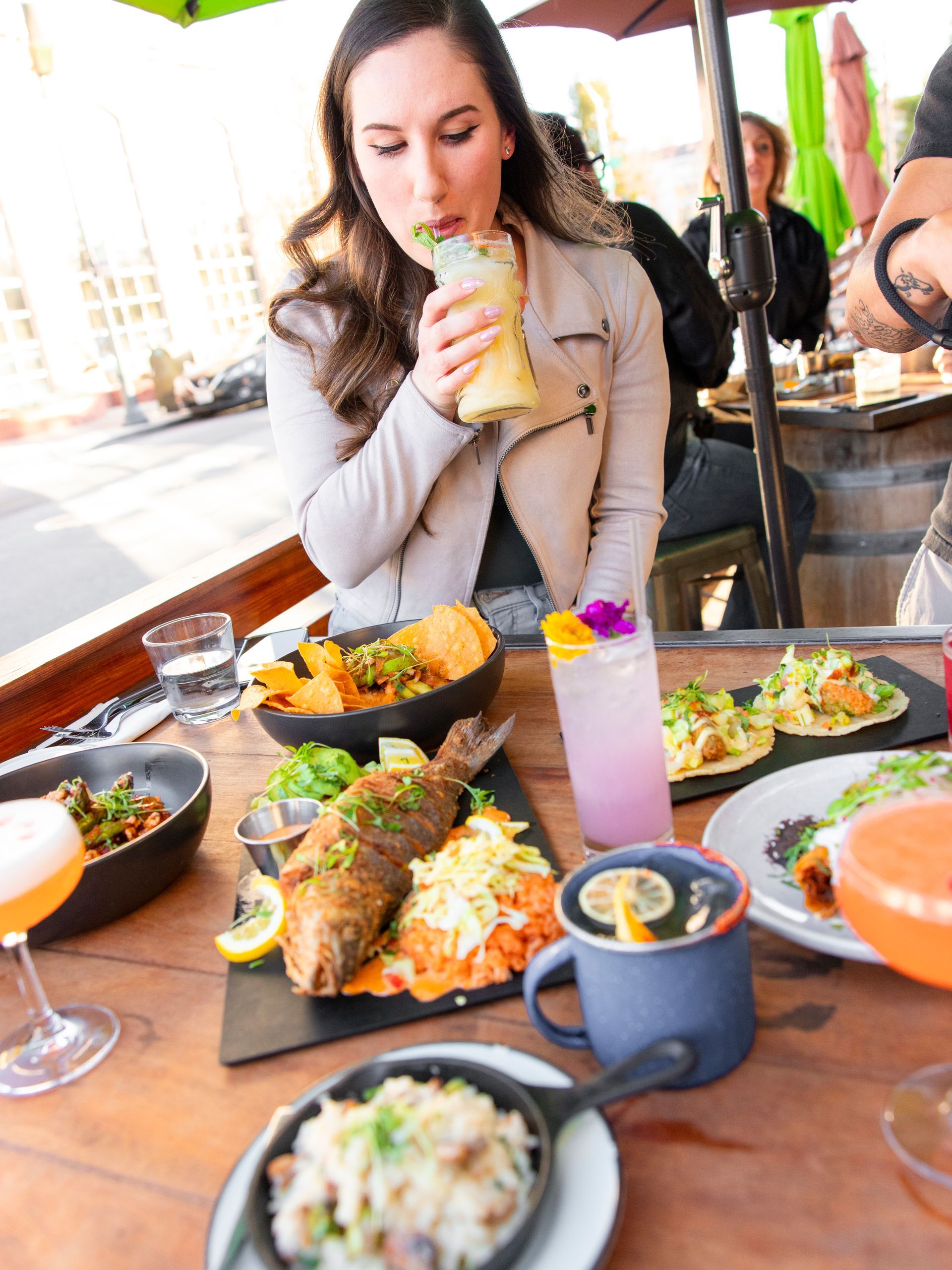 A woman is sitting at a table with plates of food and drinks.