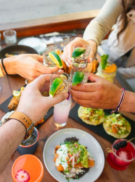 A group of people are toasting with tequila shots while sitting at a table with food.