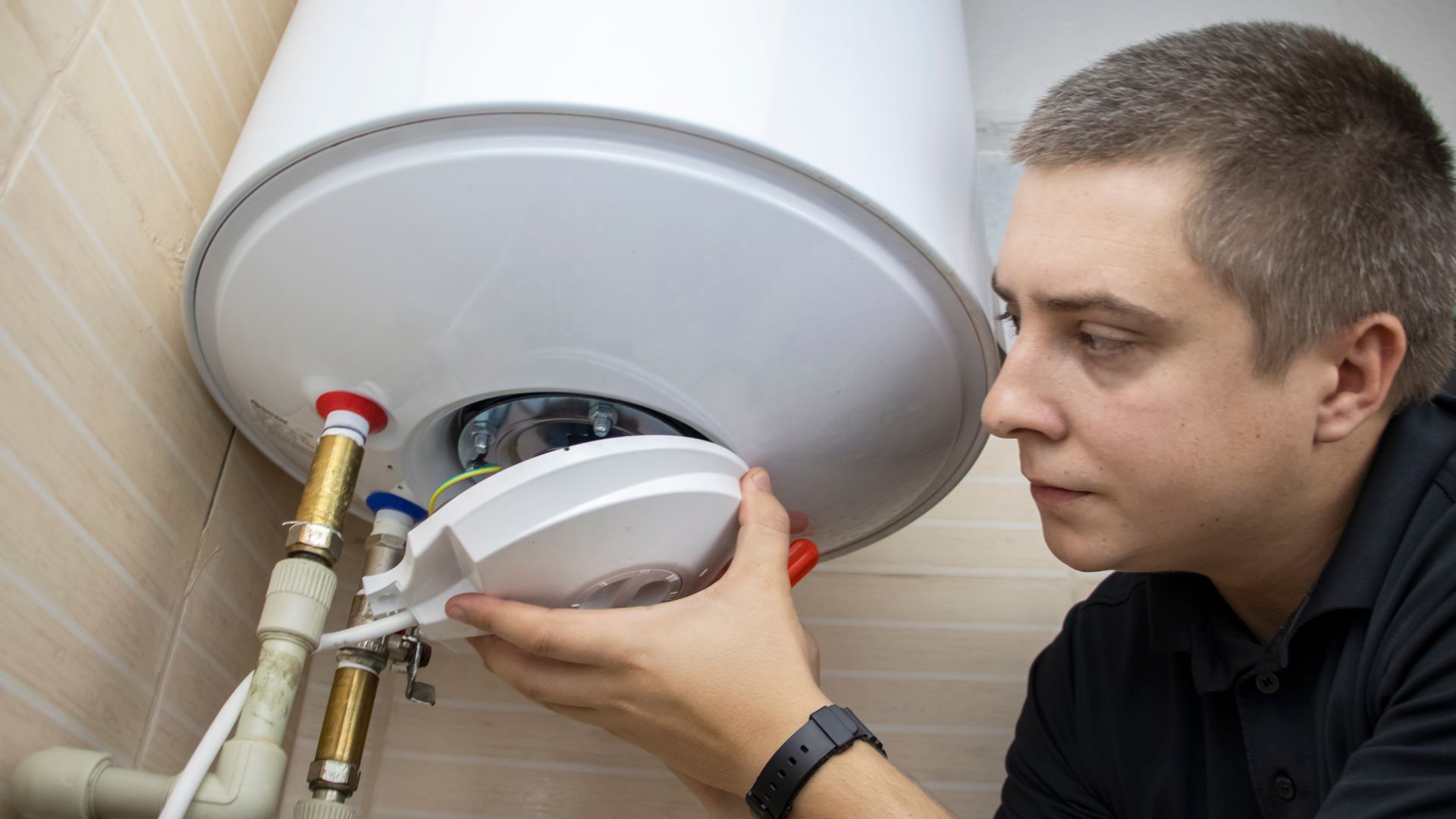 Man installing the bottom panel of a white water heater in a bathroom.