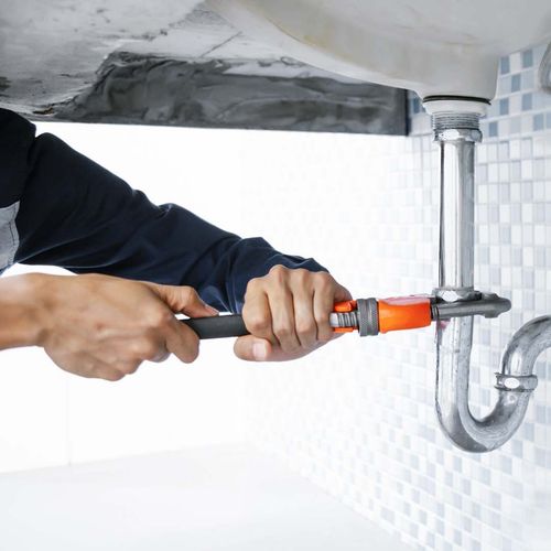 Plumber using a wrench to work on a pipe under a sink.