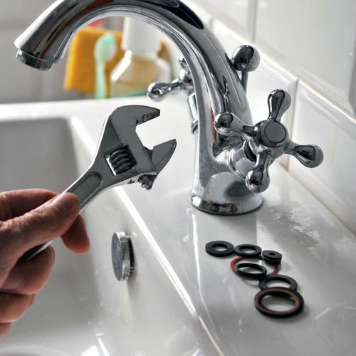 Person with wrench fixing a faucet, with replacement washers on a white sink.