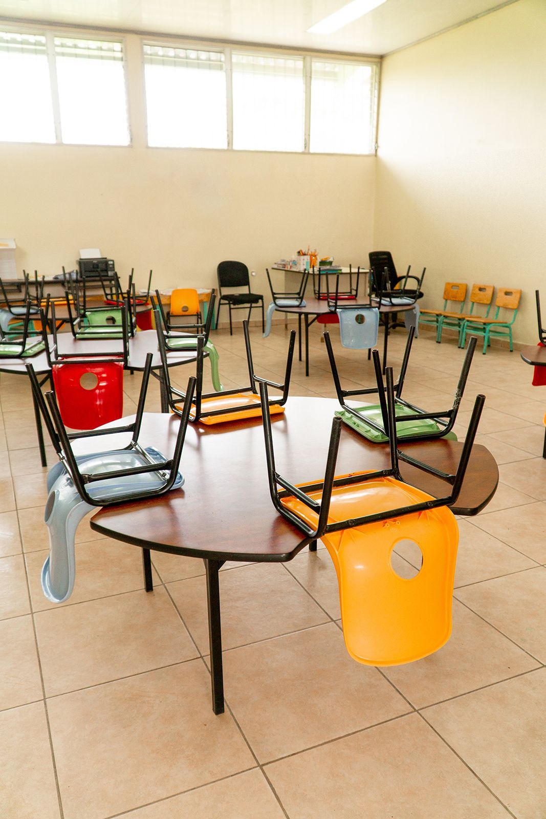 Aula con mesas y sillas volteadas. Sillas de colores rodean una mesa de madera oscura.