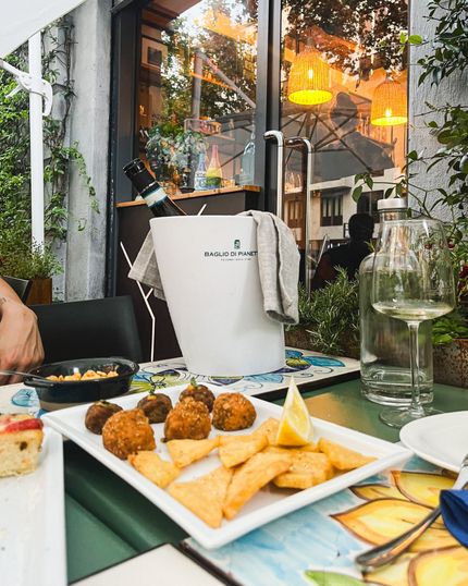 Una persona è seduta a un tavolo con un piatto di cibo e un secchio di vino.