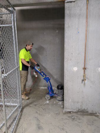 Man operating a concrete grinder to prepare an area for sealing