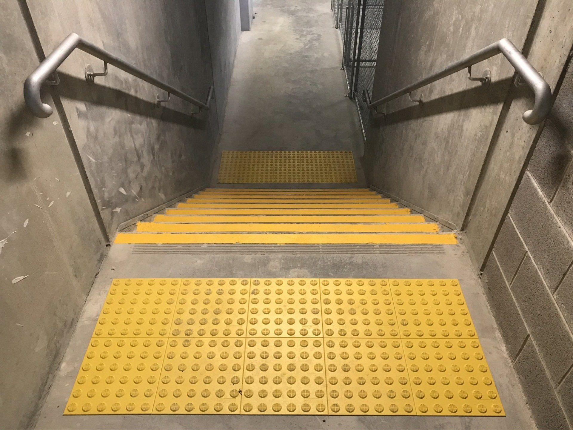 Galvanised steel fire stair handrails on both sides of a set of stairs with yellow tactiles and stair nosing