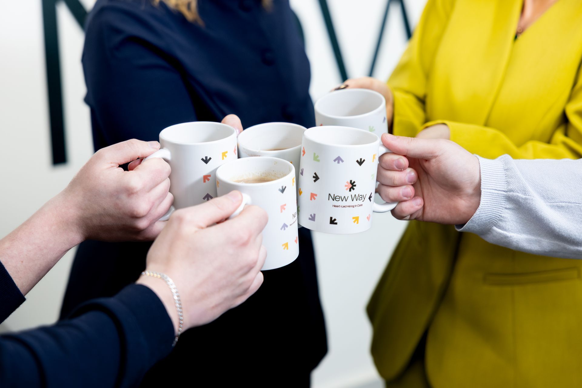 Four people clink white mugs together, with one bright yellow jacket visible.