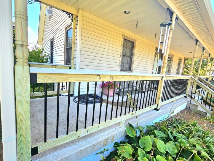 Newly constructed porch with black railings and light wood trim on a house.
