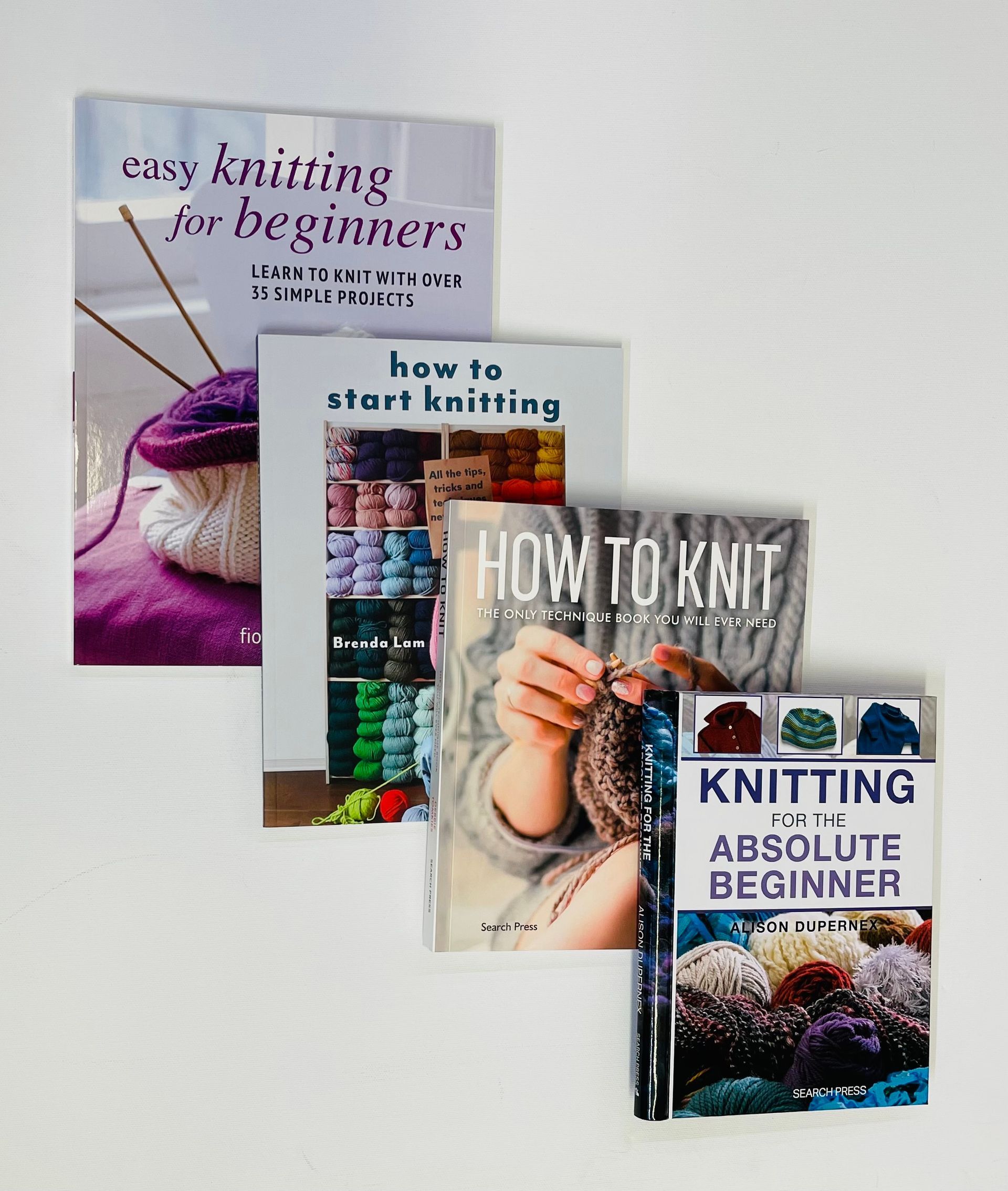 Four knitting books stacked, featuring titles like