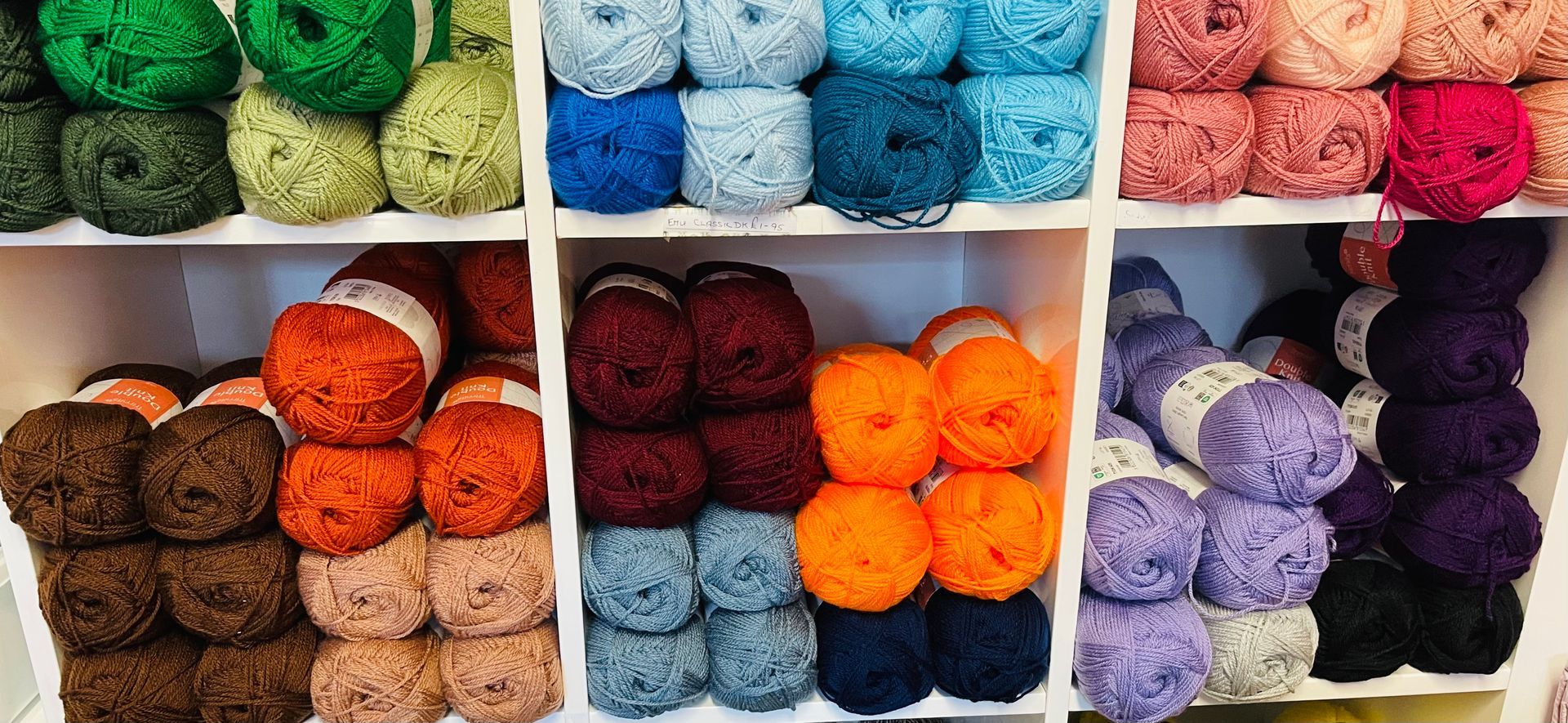 Yarn balls in various colors arranged on shelves, including green, blue, orange, brown, purple, and pink.