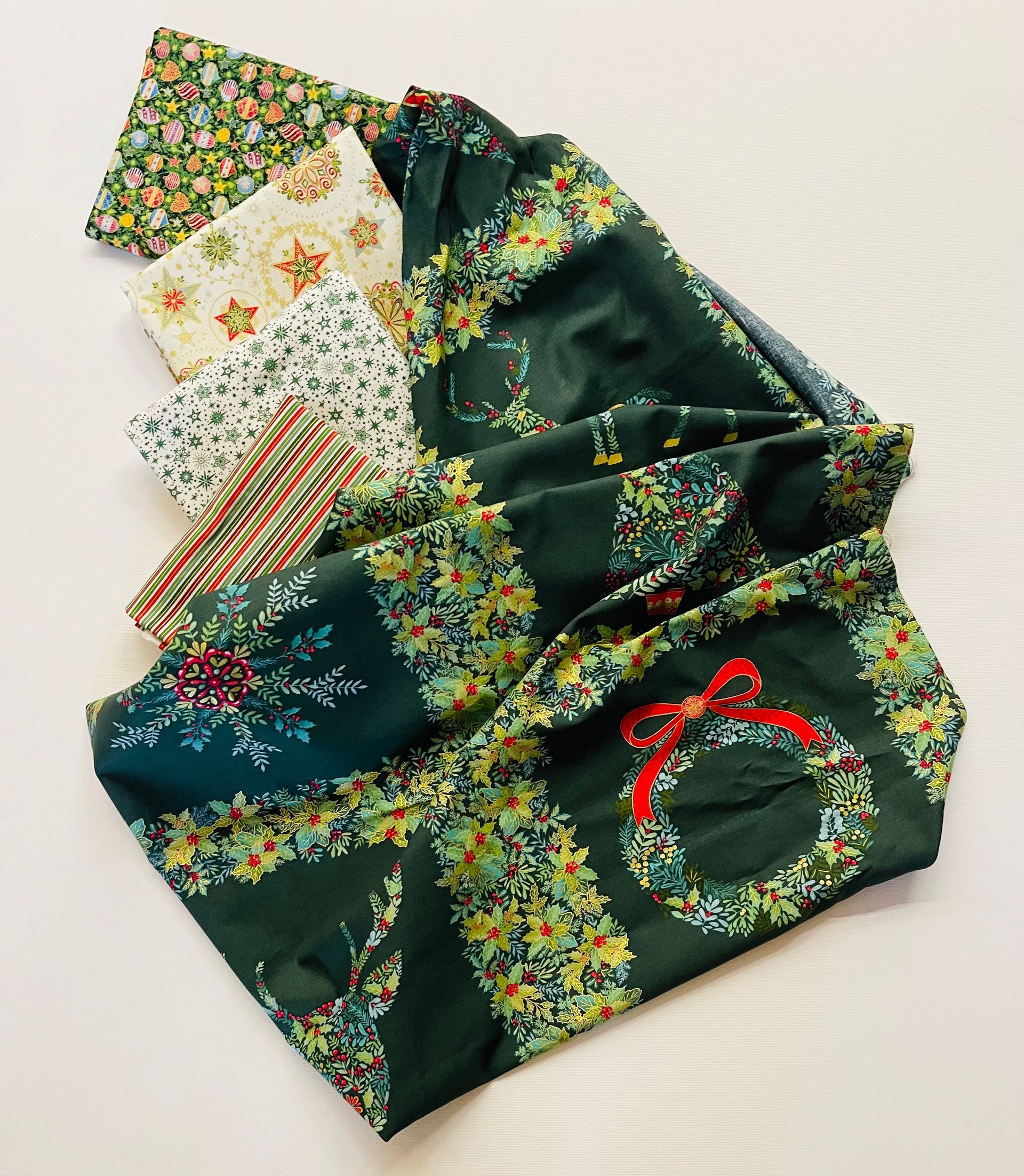 Fabric scraps and a rolled-up length of Christmas-themed fabric, mostly green with floral patterns and a wreath.