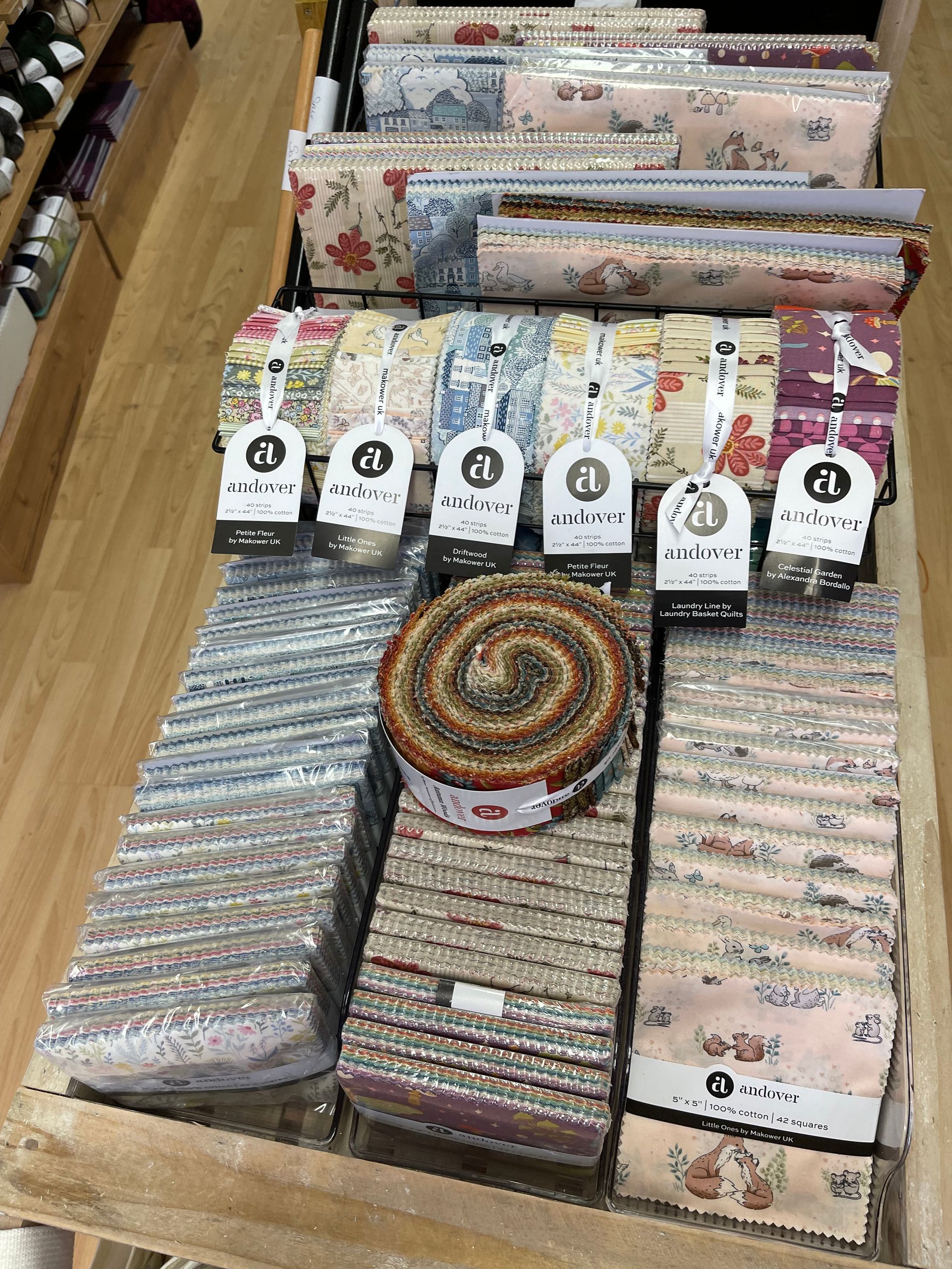 A display of folded fabric bundles and a rolled fabric jelly roll in various floral and patterned designs on a table.