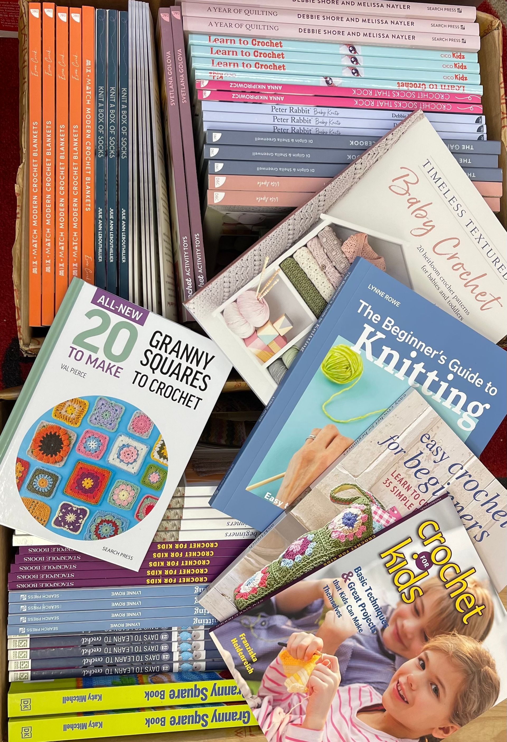 Four colorful needlework books and pattern booklets stacked on a white surface