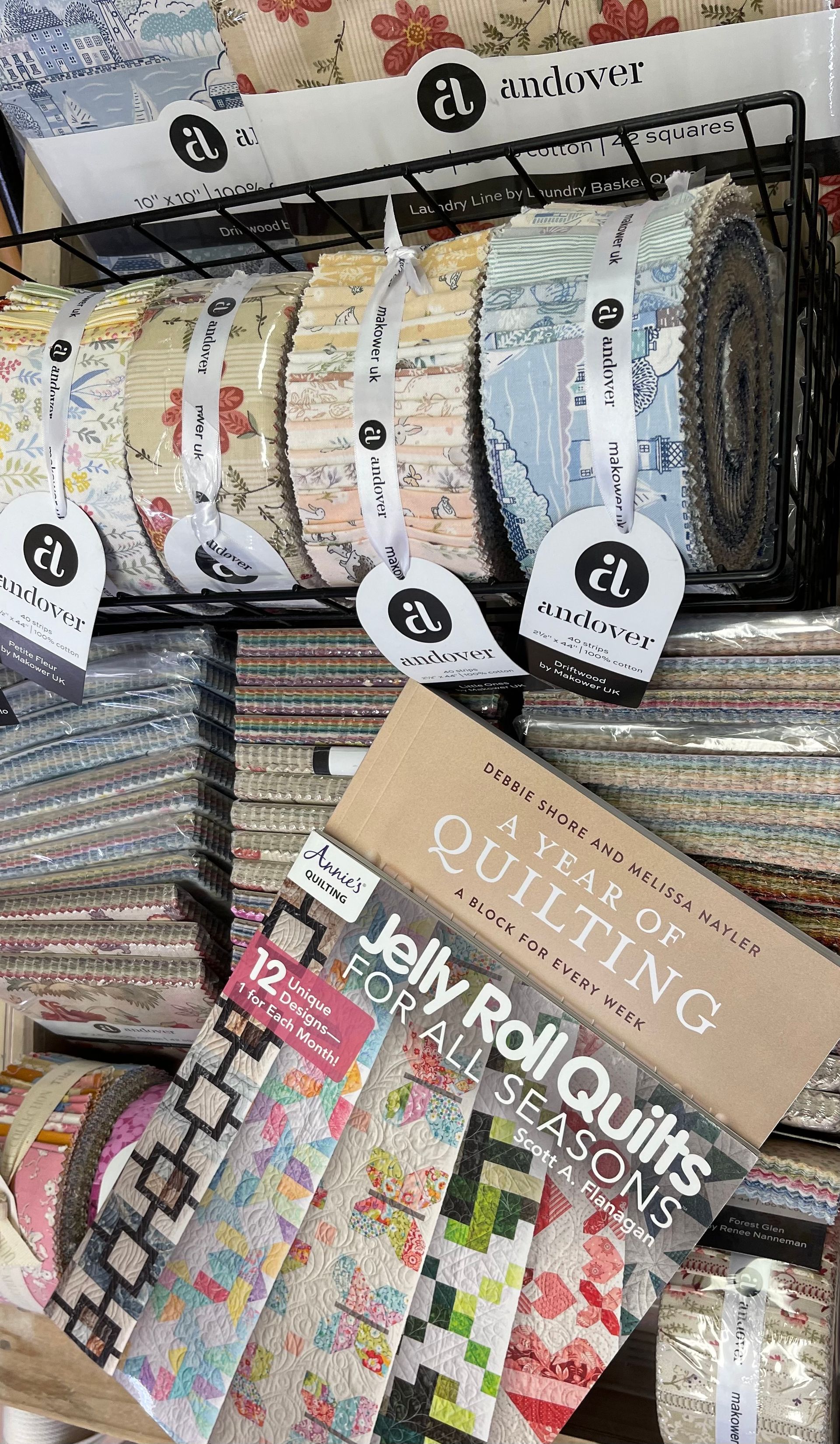 Stacked rolls of colorful patterned fabric in a store display, with a floral sample swatch on top.