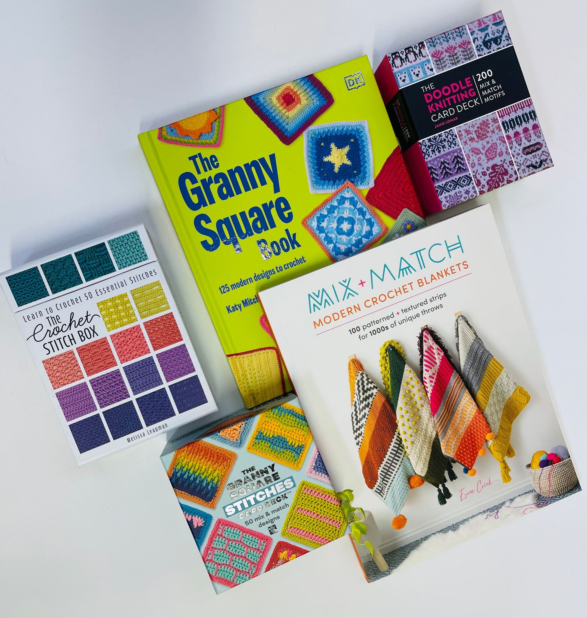 Four colorful needlework books and pattern booklets stacked on a white surface