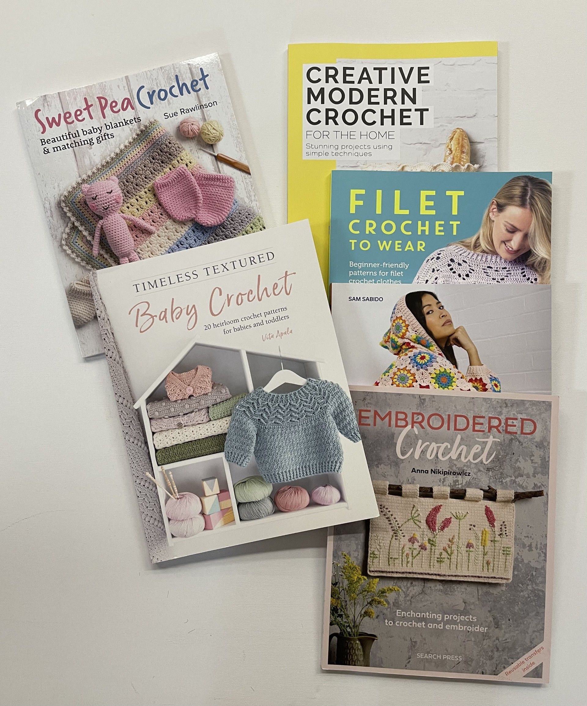 A group of crochet books are sitting on top of each other on a table.