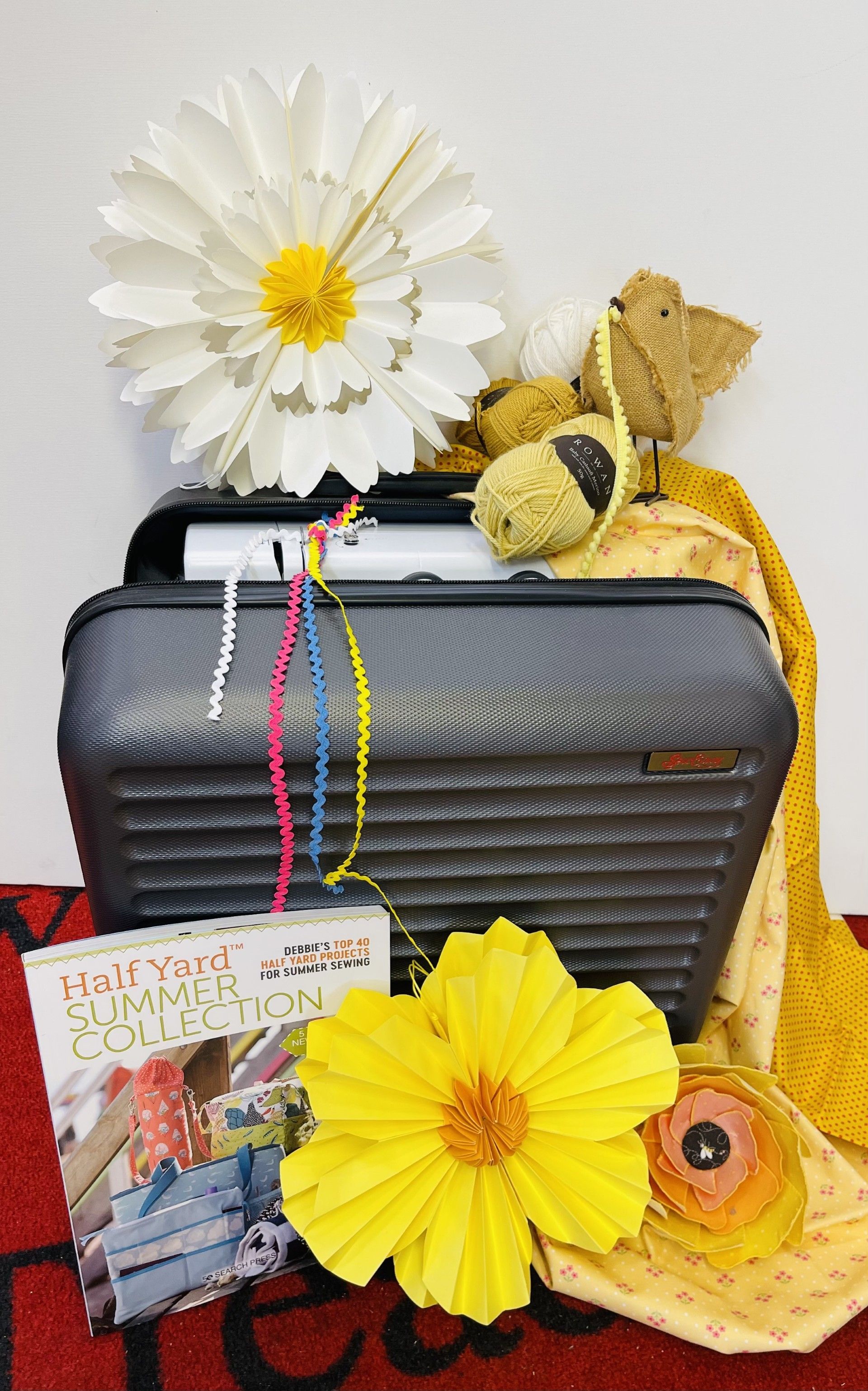 A suitcase is surrounded by flowers and a teddy bear.