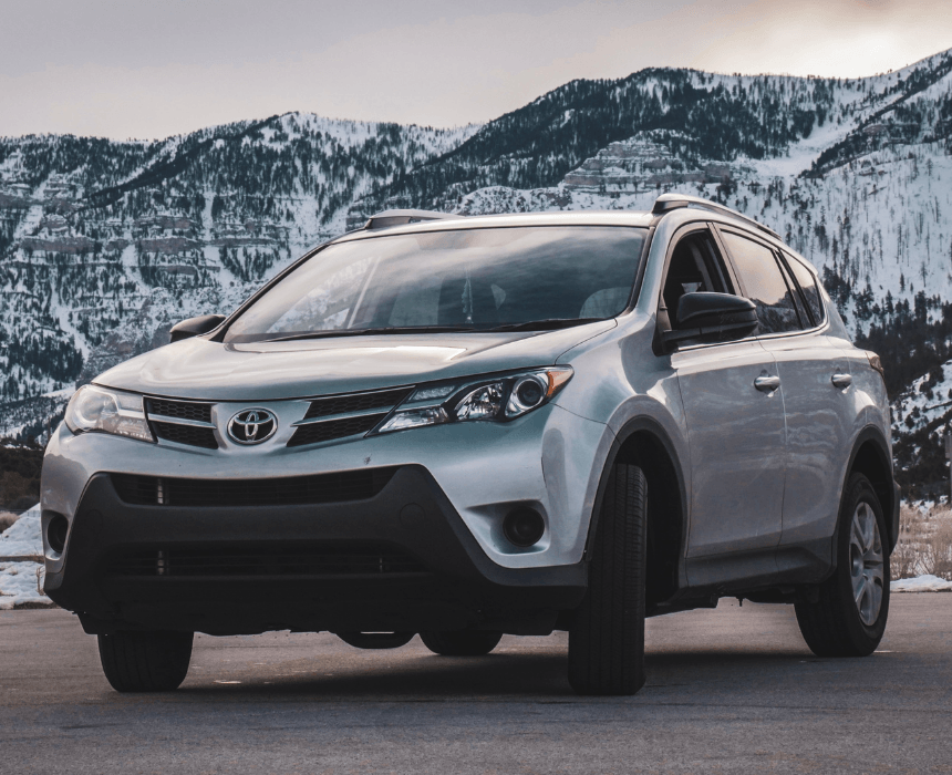 A silver toyota rav4 is parked in front of snow covered mountains.