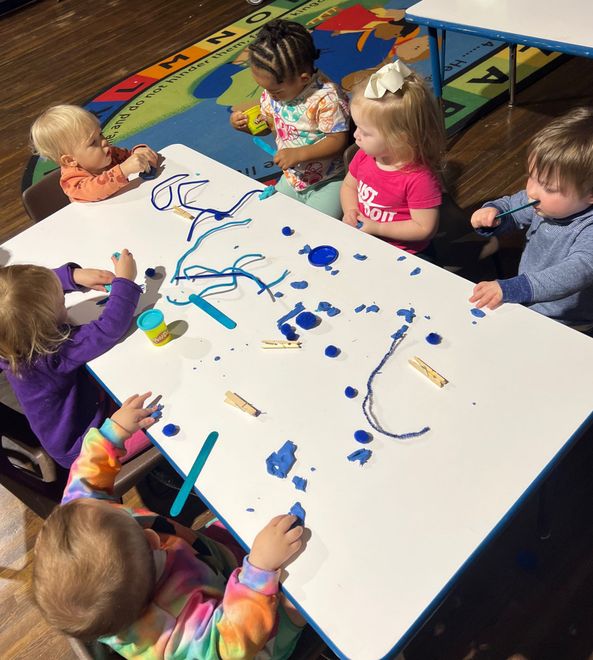 a group of children are sitting at a table playing with clay