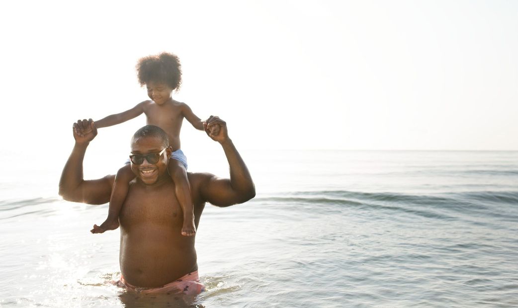 A man is carrying a child on his shoulders in the ocean.