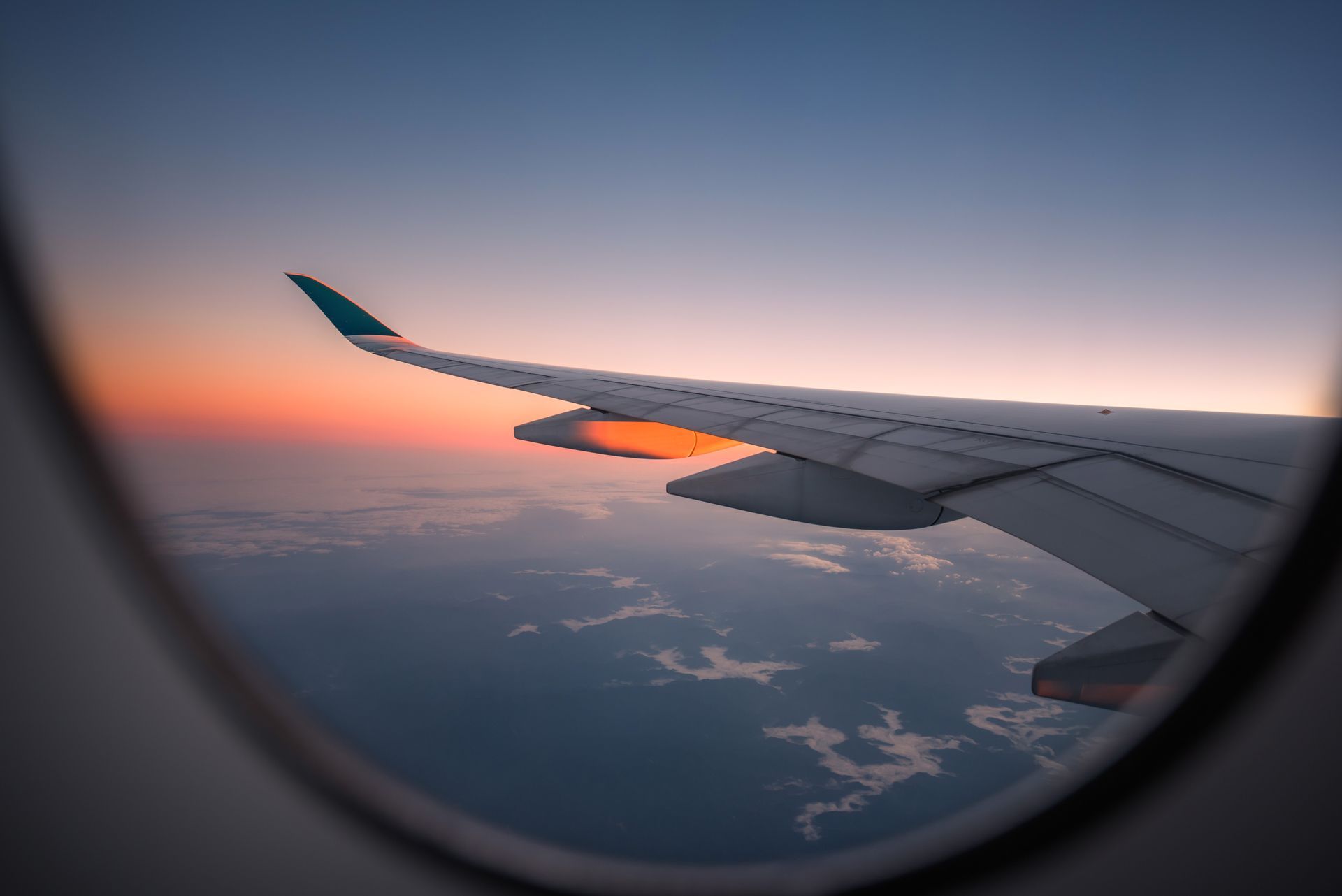 The wing of an airplane is visible through the window at sunset.
