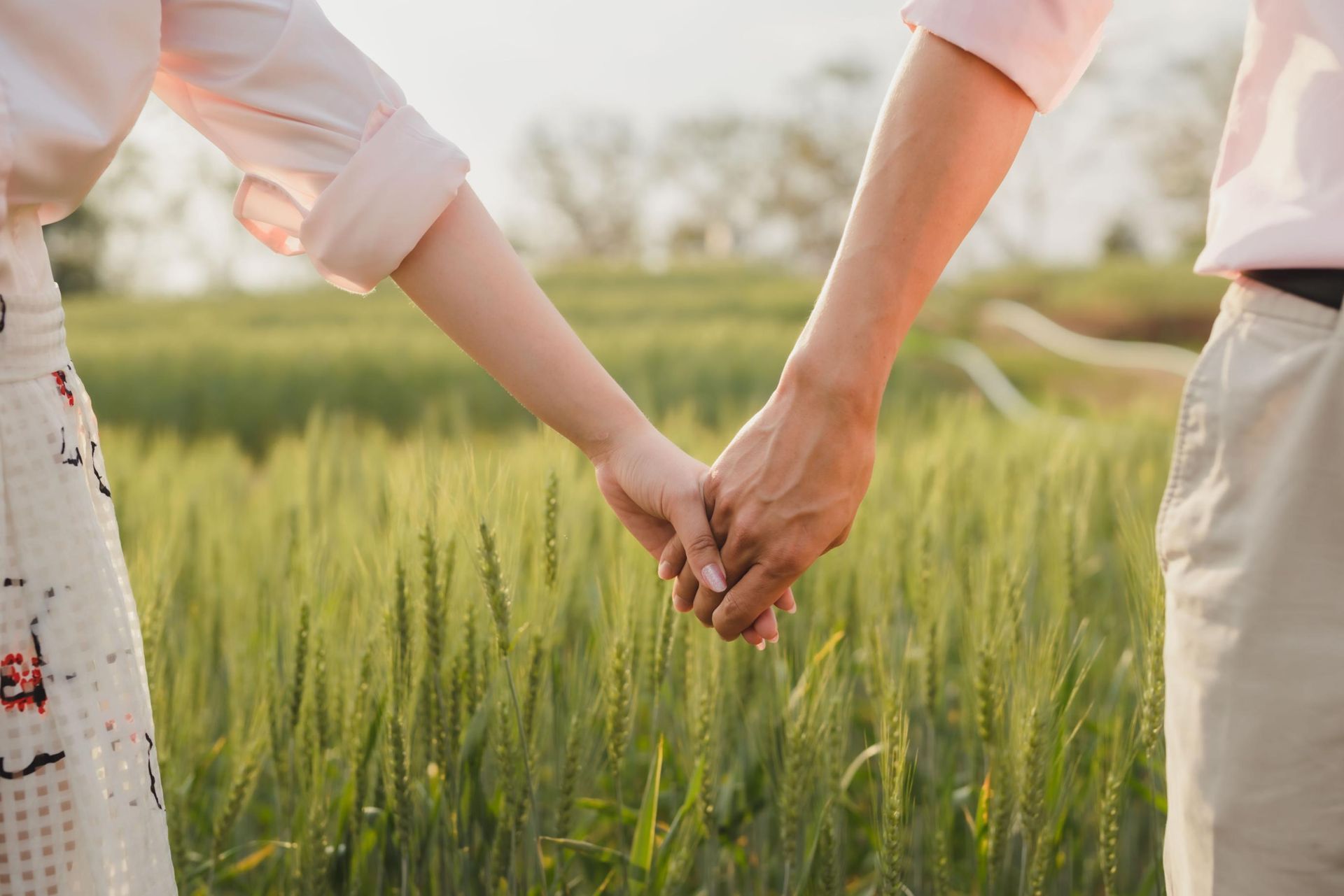 Couple holding hands in a field of wheat, with sunlight casting shadows.