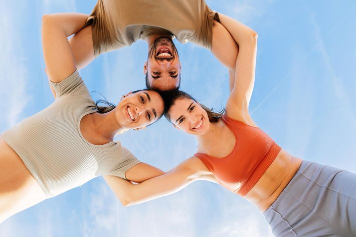 Three smiling people, heads together forming a circle, arms interlocked against a blue sky.