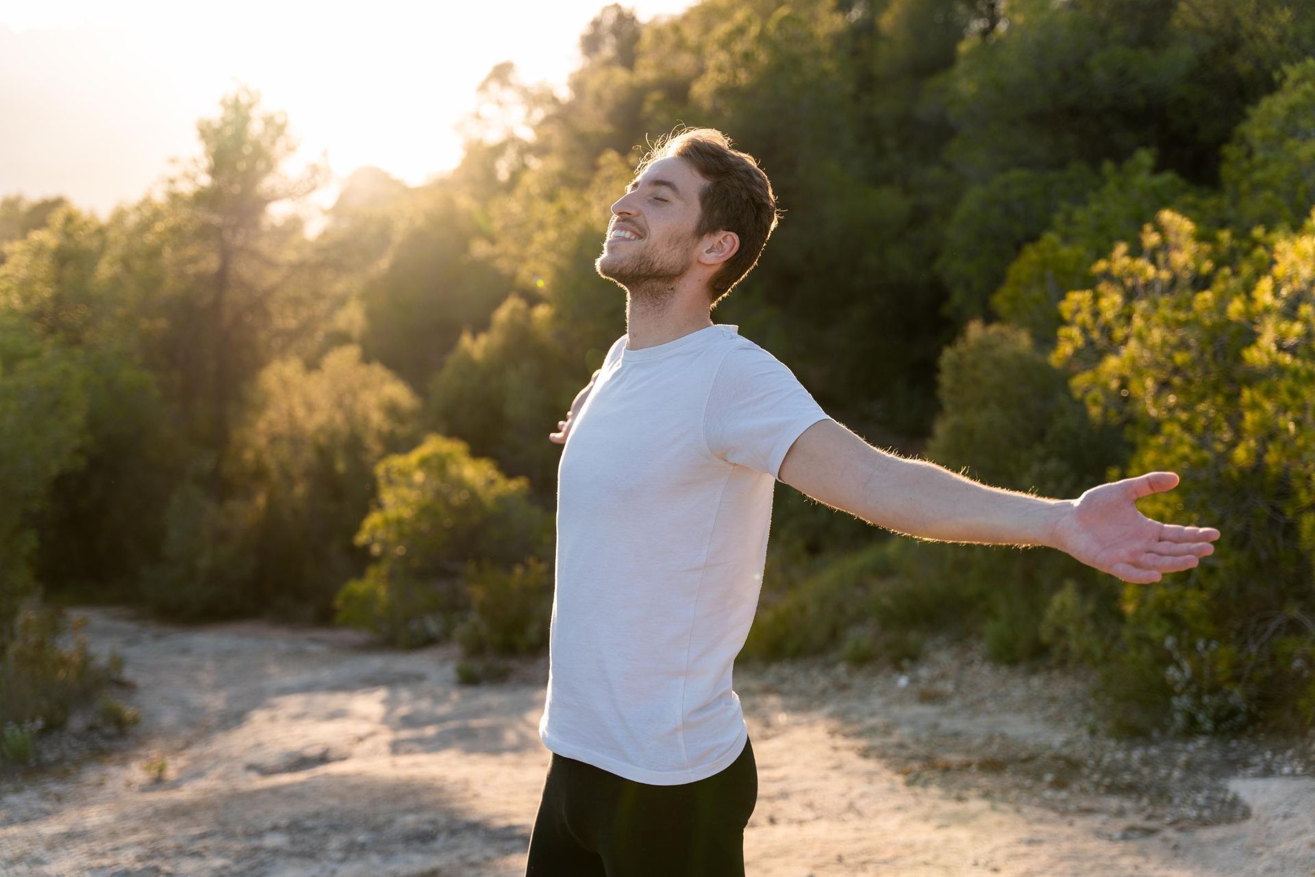 Man with arms outstretched, smiling, enjoying the sunlight in a forest.
