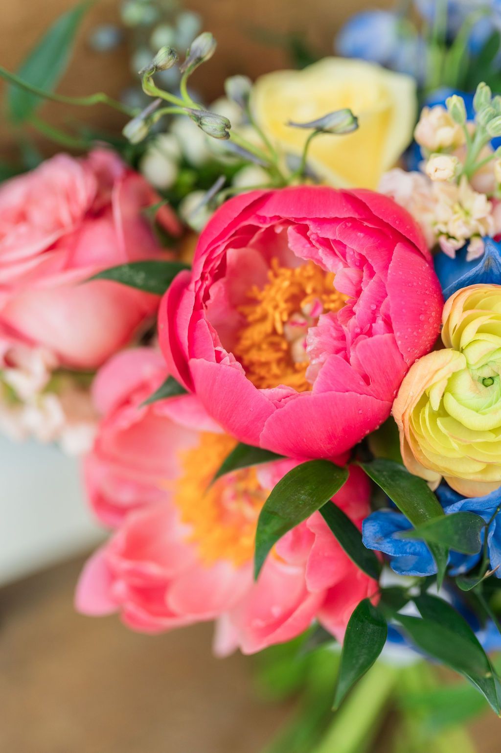 Close-up of a bouquet with pink peonies, yellow ranunculus, and blue delphiniums.
